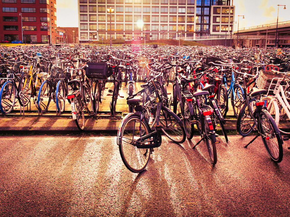 Thousands of parked bicycles filling a station square at sunset with office buildings behind, Amsterdam