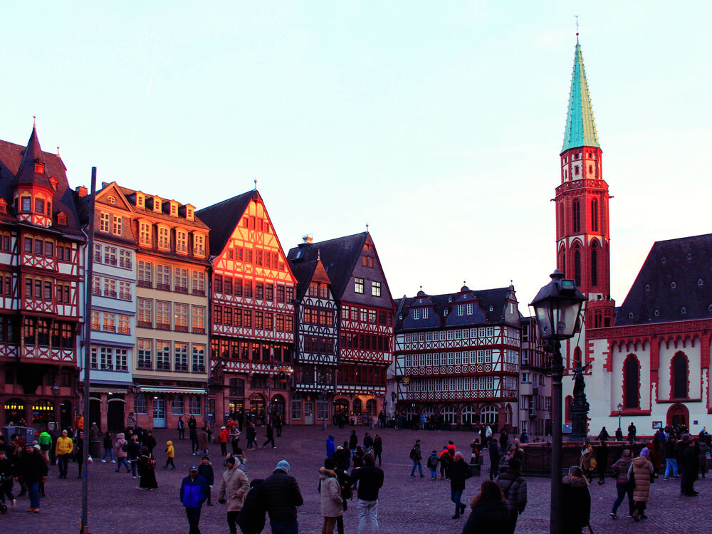 Half-timbered gabled houses and a church spire around the Römerberg square at dusk with crowds, Frankfurt